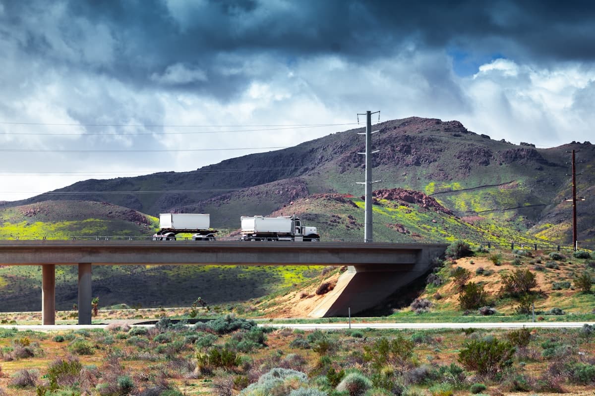 Trucks crossing highway bridge with Kern County mountains and dramatic sky in background