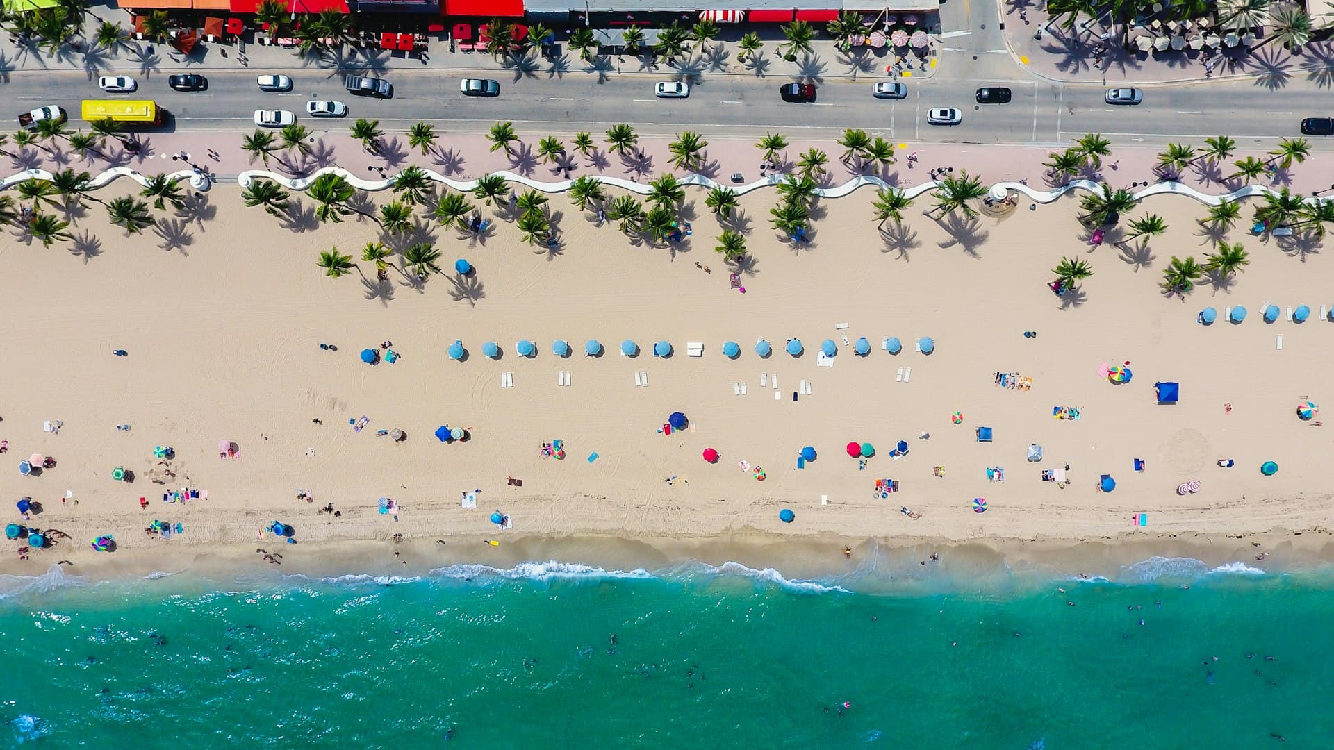 Aerial view of Fort Lauderdale Beach with palm trees, beach umbrellas, and A1A beachfront road
